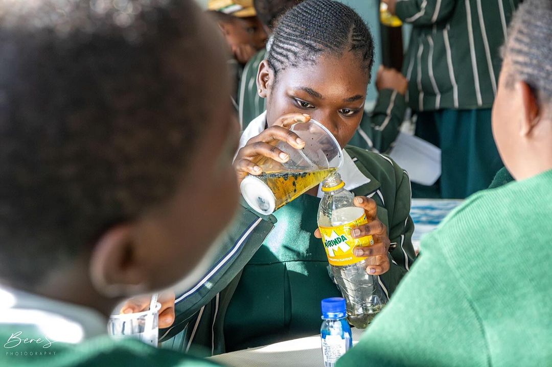 A student in a classroom carefully pouring a liquid from a cup into a soda bottle