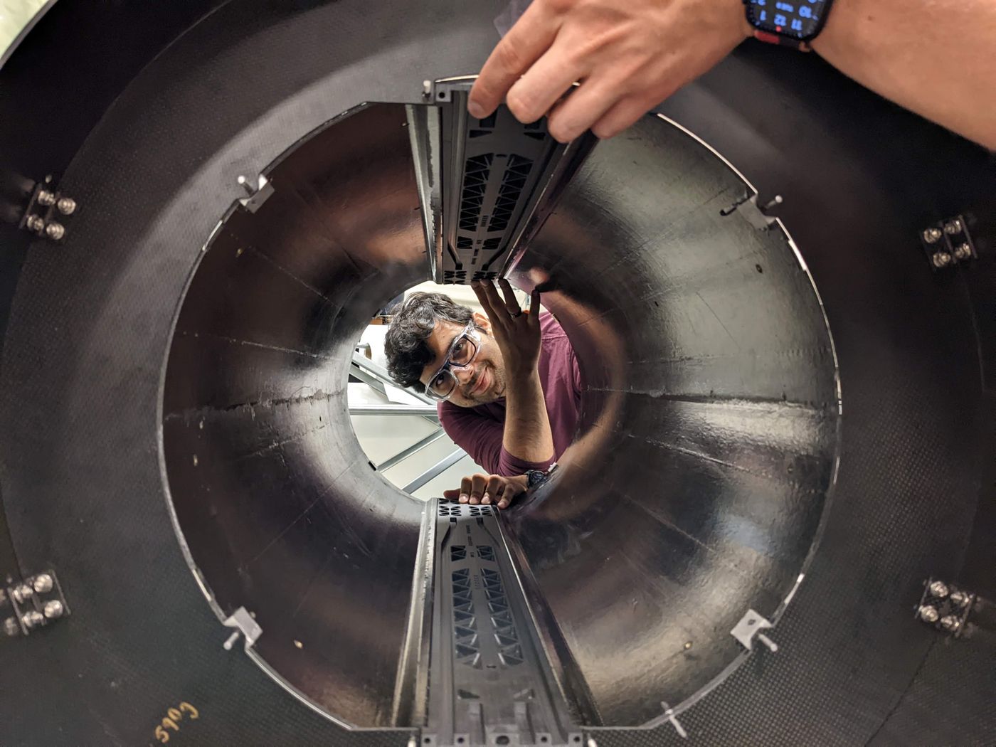 man in safety glasses looking at the inside of a large composite tube