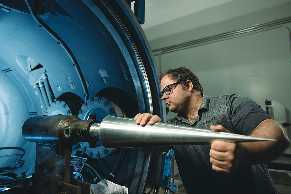 A man mounts a pointed steel cone horizontally on a platform inside the HYPULSE test section