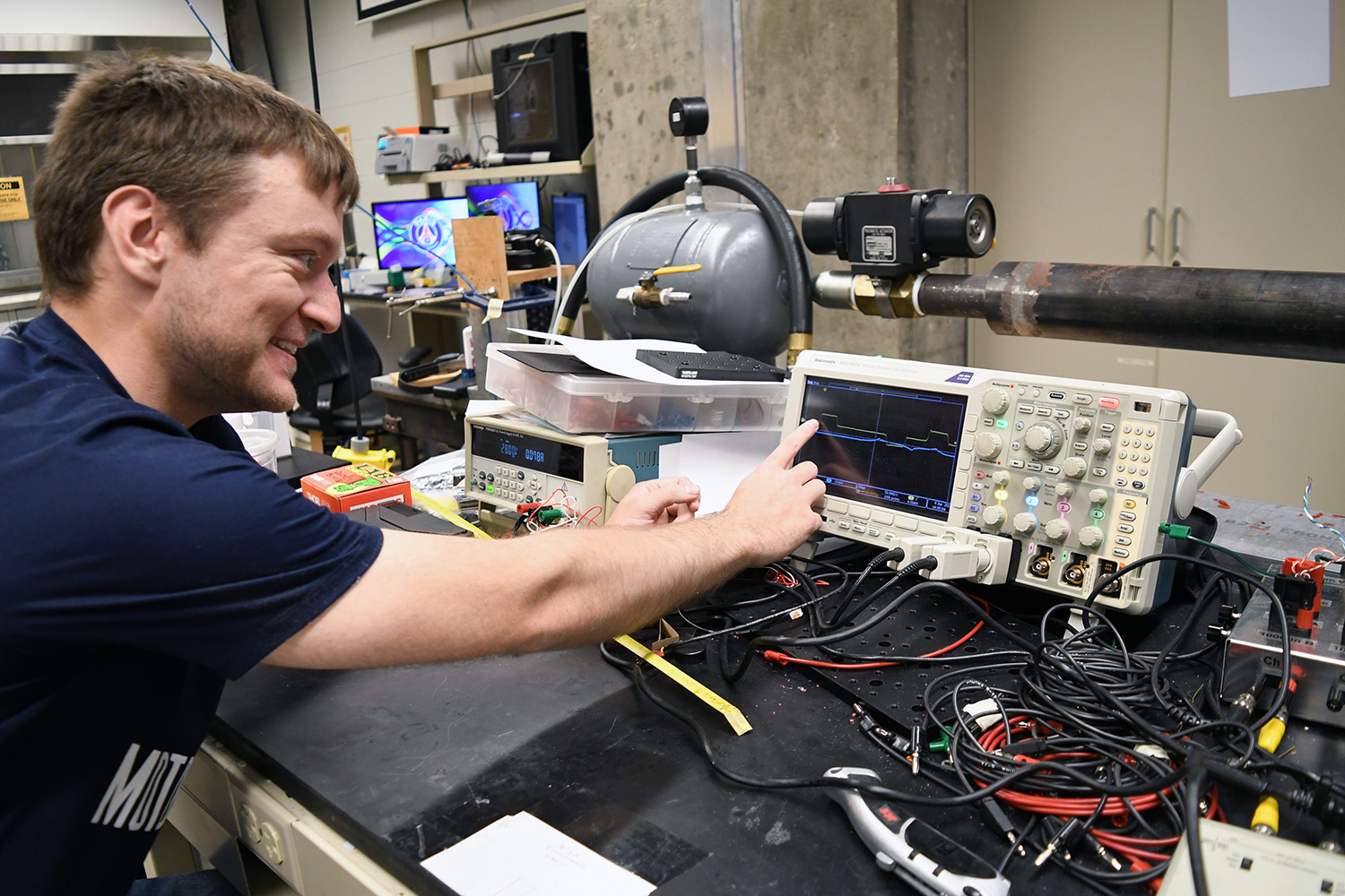 Tyler Dillard pointing at the screen of an oscilloscope in Purdue's Impact Science Lab