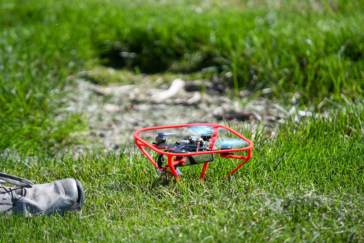 A small drone sitting in the grass spins its propellers