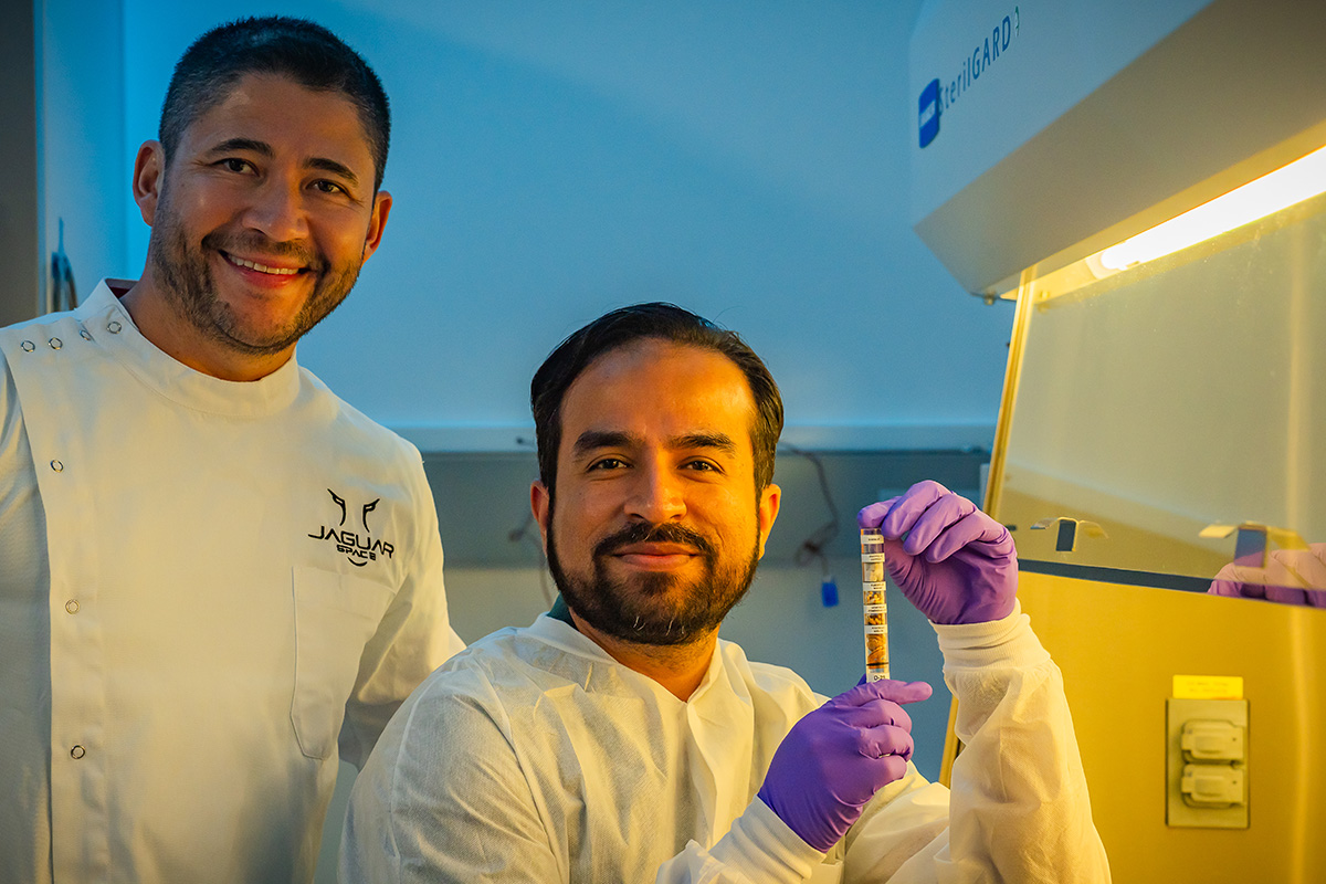 Mahhad Nayyer holding a small container containing seeds from various nations. Luis Zea stands behind Nayyer.
