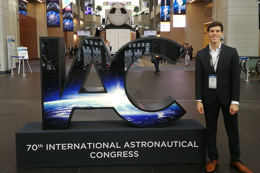 Roy Ramirez standing next to the entry sign at the 2019 International Astronautical Congress.