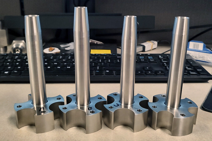 Four small metal cylinders with nozzles, mounted on bases, sitting on a desk