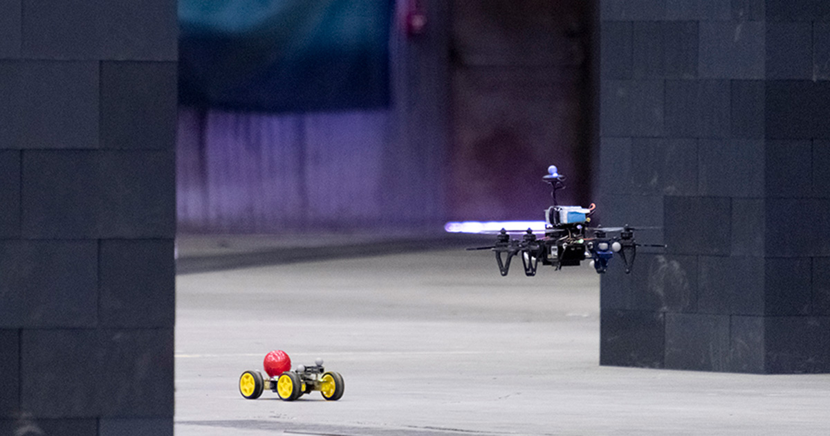 A drone chasing a small car across a concrete floor