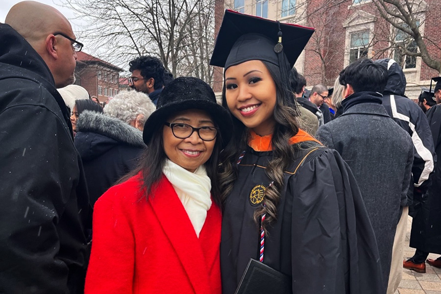 Ellen Nguyen standing outside with a graduation gown on a snowy day, her mom beside her.