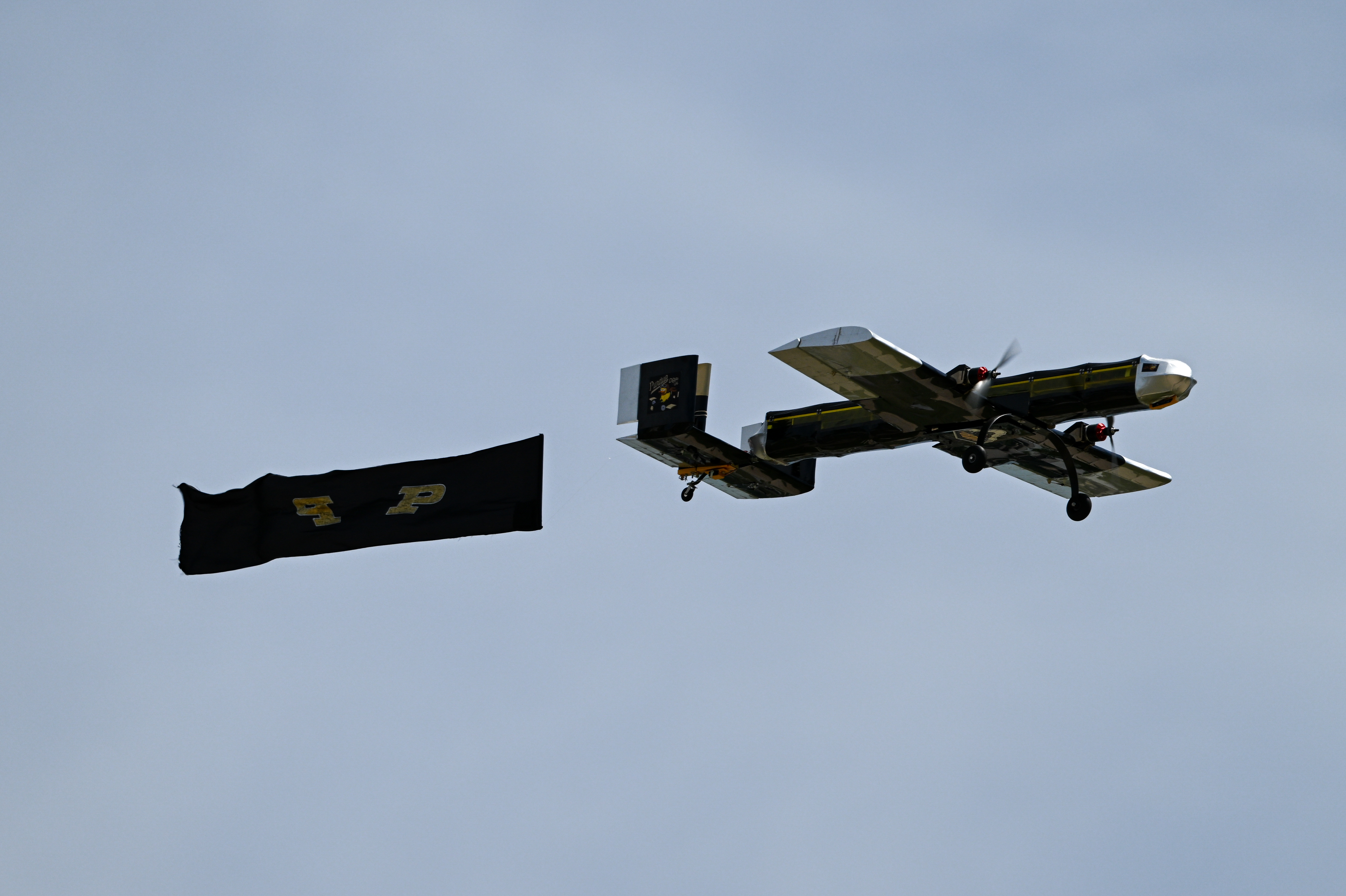 Team's plane flying in the sky with Purdue banner streaming behind it