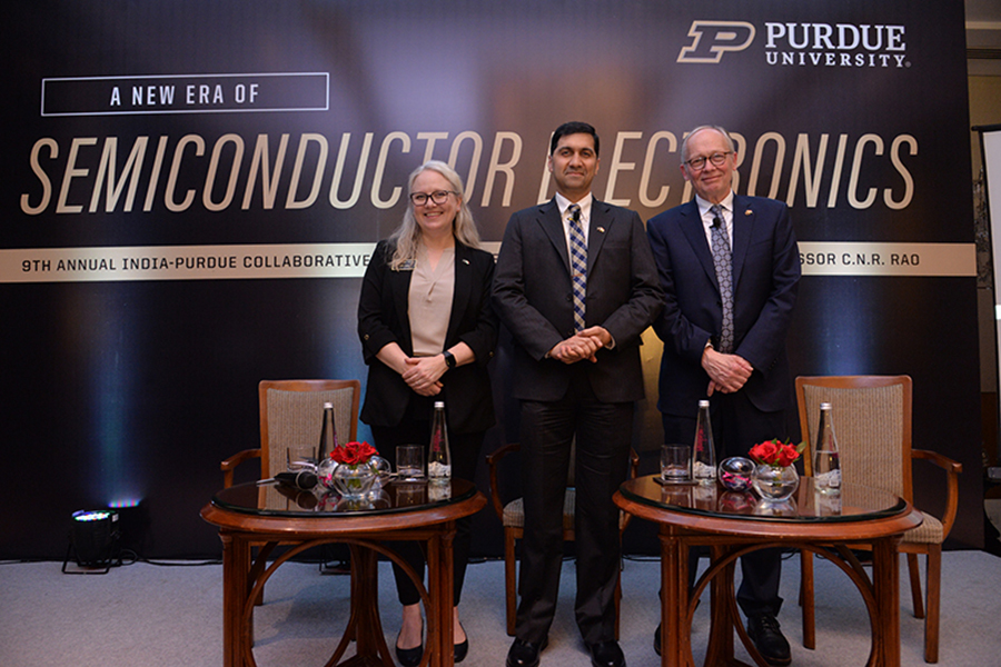 Heidi Arola, Vijay Raghunathan and Mark Lundstrom stand in front of  a purdue branded backdrop, there are tables with bottles of water in the foreground, all are smiling