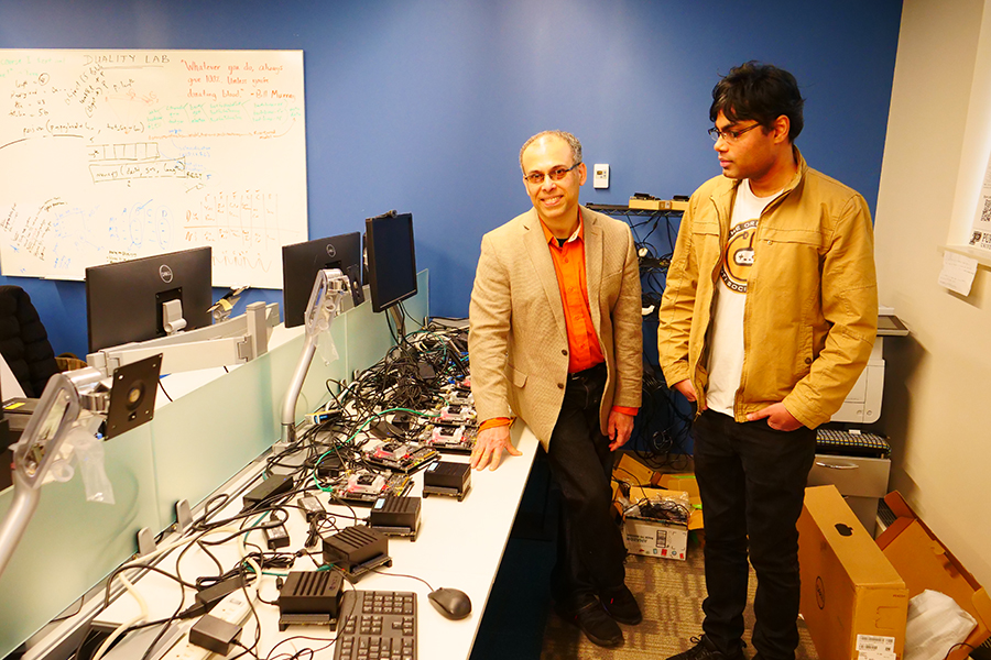 Saurabh Bagchi, Professor of Electrical and Computer Engineering, and Vishal Shrivastav, Assistant Professor of Electrical and Computer Engineering, are in the lab with equipment such as mobile GPUs and programmable routers and switches. They are standing in a lab surrounded by computer stations and the various parts used for their research.