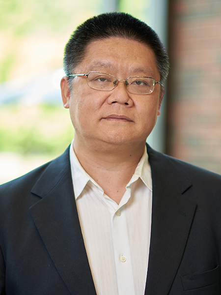 Portrait of Husheng Li. He is wearing a white button up shirt with a suit jacket and standing in the atrium of MSEE.