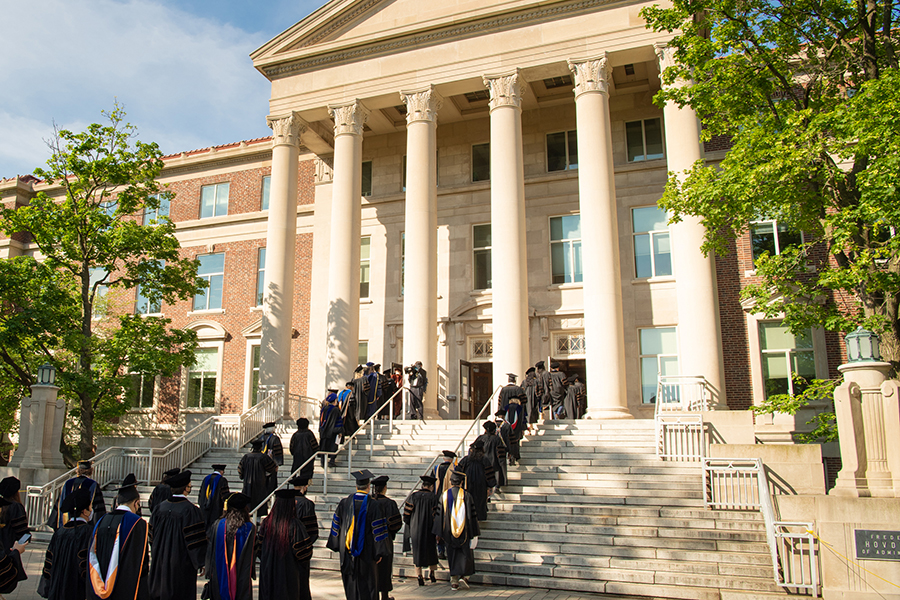 University stock photo of students dressed in their commencement hats and gowns, walking up the steps of Hovde Hall