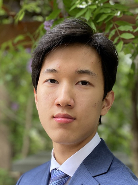 Portrait of student Shihun Kim. He is wearing a suit jacket and tie and standing in front of some greenery.