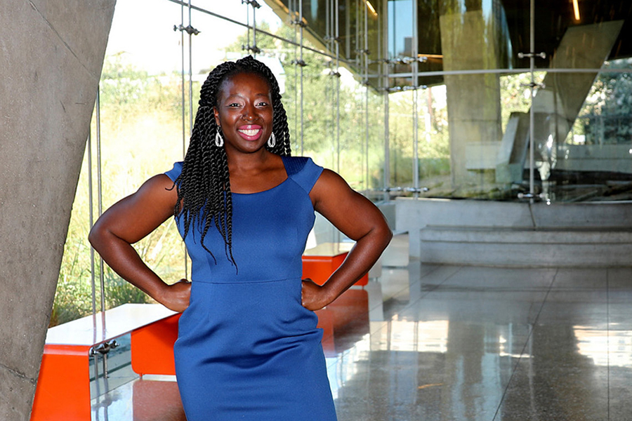 Afua Bruce stands in a blue dress inside a modern building.