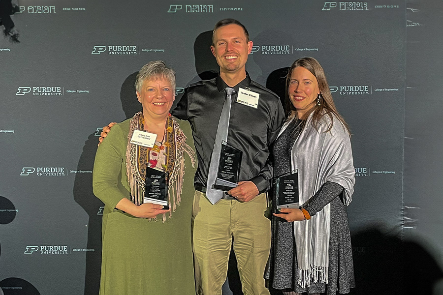 Mary Ann Satterfield, Jordan Gilman, and Jamie Seadeek gather for a group photo standing in front of a Purdue Engineering backdrop. All are holding their trophies.