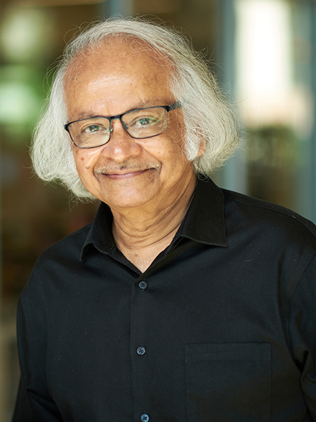 Portrait of Supriyo Datta. He has chin length white hair, wears glasses, and is wearing a black button up shirt.