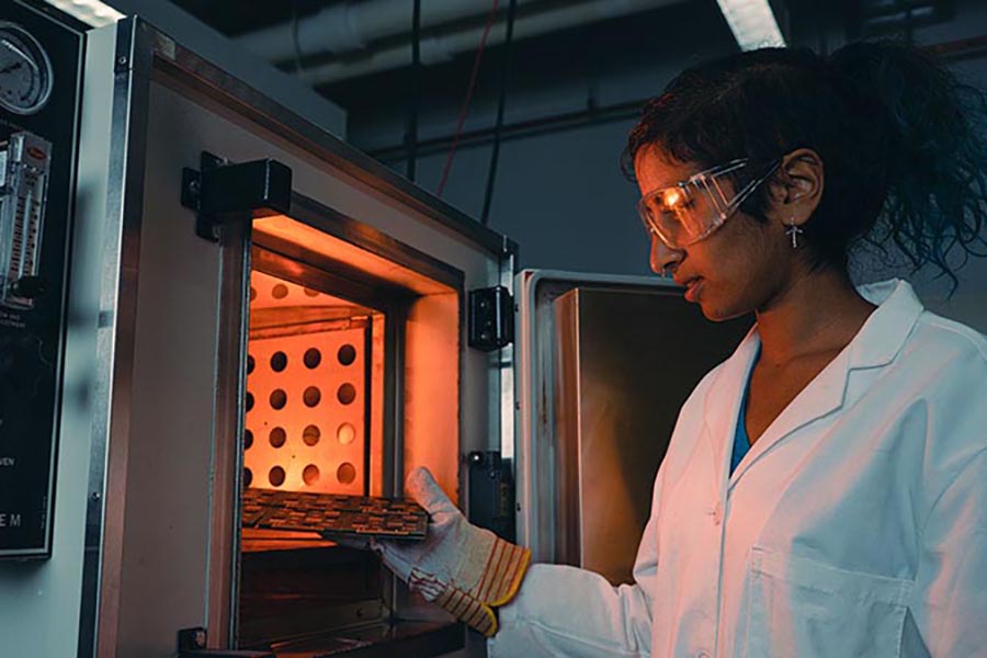 Purdue student Anna Murray places printed circuit board samples into an oven to test for stability and other important qualities in electronic components. She is wearing protective gloves and goggles along with a lab coat.
