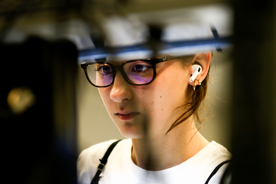 A young woman wearing glasses an airpods is looking at a screen in an electrical and computer engineering laboratory.