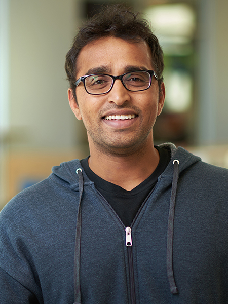 Professor Aravind Marchiry poses for a portrait in the atrium of the MSEE building. He is wearing glasses, a black t shirt, and a gray zip up sweatshirt.