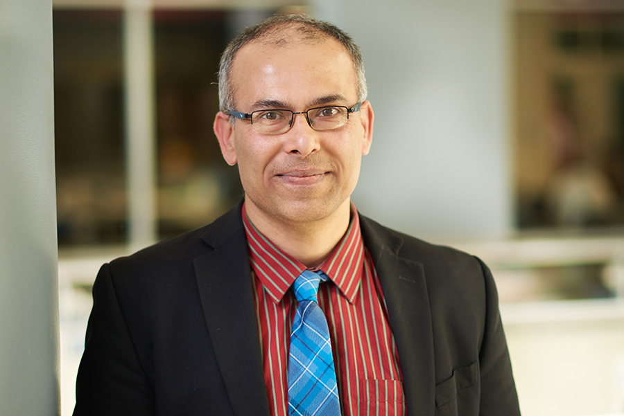Professor Saurabh Bagchi poses for a portrait in the atrium of the MSEE building. He is wearing glasses, a red shirt, blue tie, and dark suit jacket.