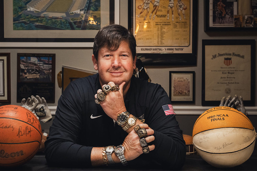 Chris Pate, wearing multiple championship rings and watches, poses for a photo with his large Purdue memorabilia collection.