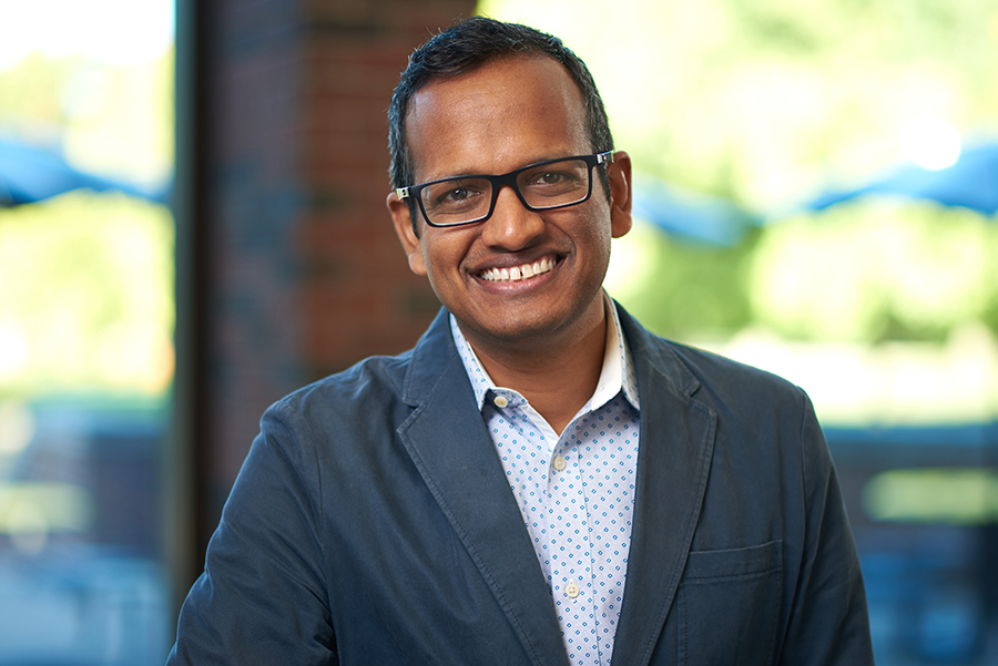 Portrait of Milind Kulkarni. He is wearing a dark gray jacket, a button up shirt, and glasses.