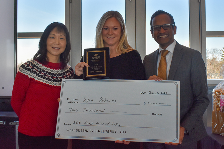 Dan Jiao, Kyra Roberts, and Milind Kulkarni pose for a photograph at the staff recognition luncheon. Kyra is holding a plaque while Dan and Milind present a large check.