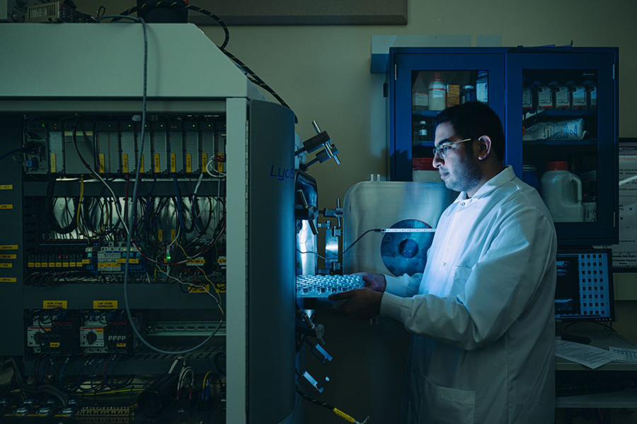 Ahmad Darwish, dressed in a lab coat, slides a tray of vials into a machine.