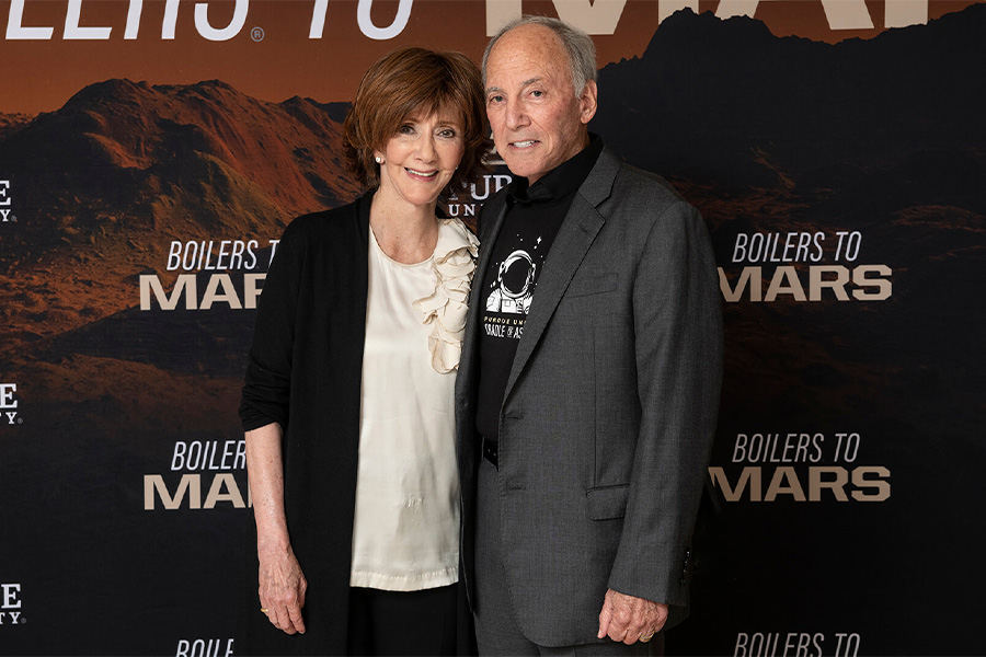 A man and woman stand together in front of a wall displaying the phrase Boilers to Mars