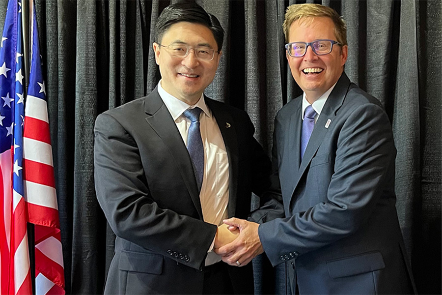 Two men dressed in suits shake hands against the backdrop of an American flag, illustrating a formal agreement