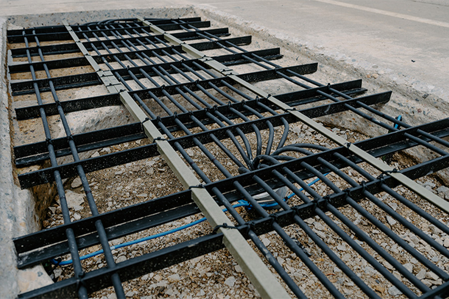 Metal rebar grid installed in a concrete trench, preparing for road or infrastructure construction. The scene conveys progress and industrial precision.