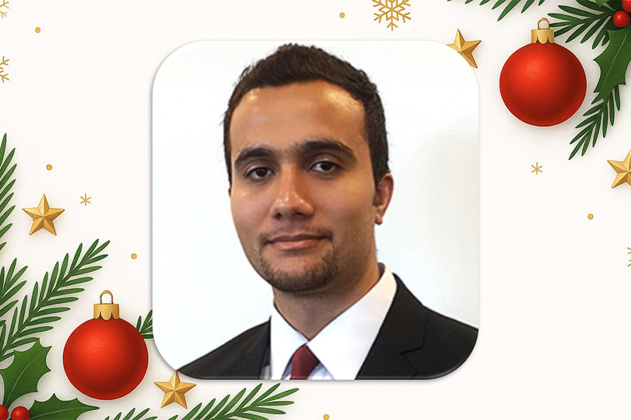 Portrait of a person in a suit and tie on a festive, holiday-themed background with red ornaments, golden stars, and green pine branches.