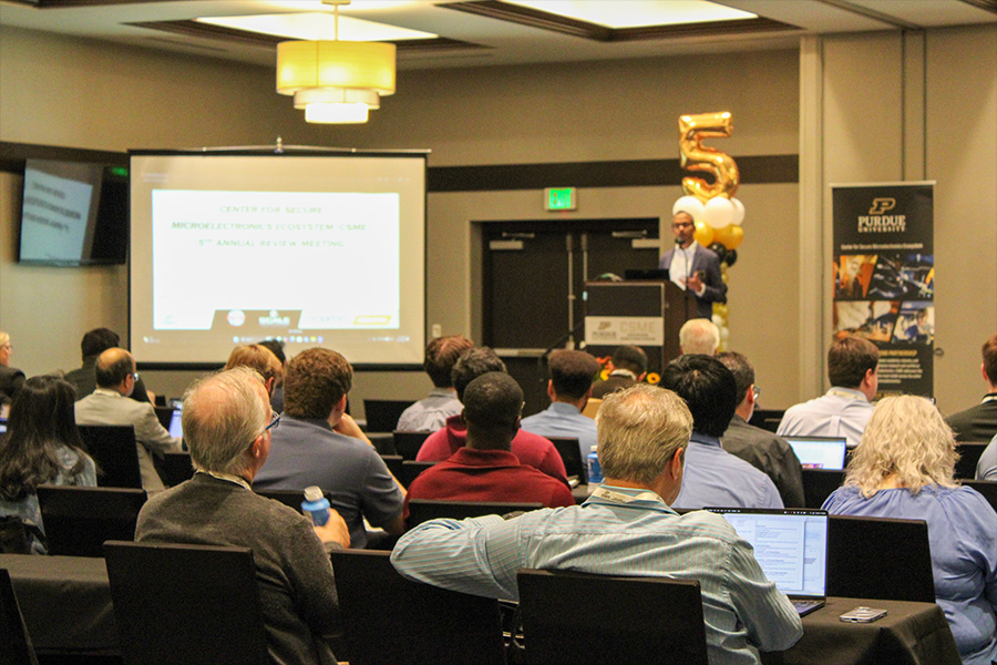 Attendees listen to a presentation during the Purdue Center for Secure Microelectronics Ecosystem (CSME) fifth annual review, with a gold balloon shaped like the number five marking the center's anniversary.