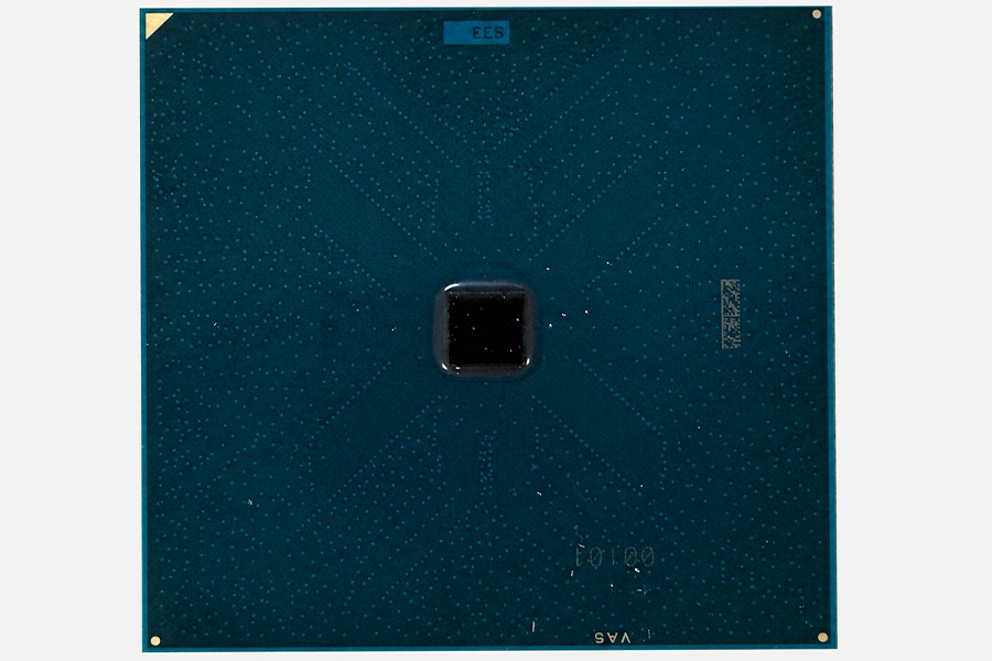 Close-up of a square teal integrated circuit package with a small black chip at the center, shown against a plain white background.