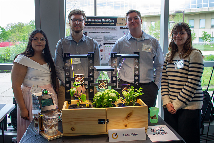 Four students present a Grow Wise autonomous plant care project with a smart indoor garden, sensors, grow lights, control electronics, and leafy herbs at an engineering showcase.