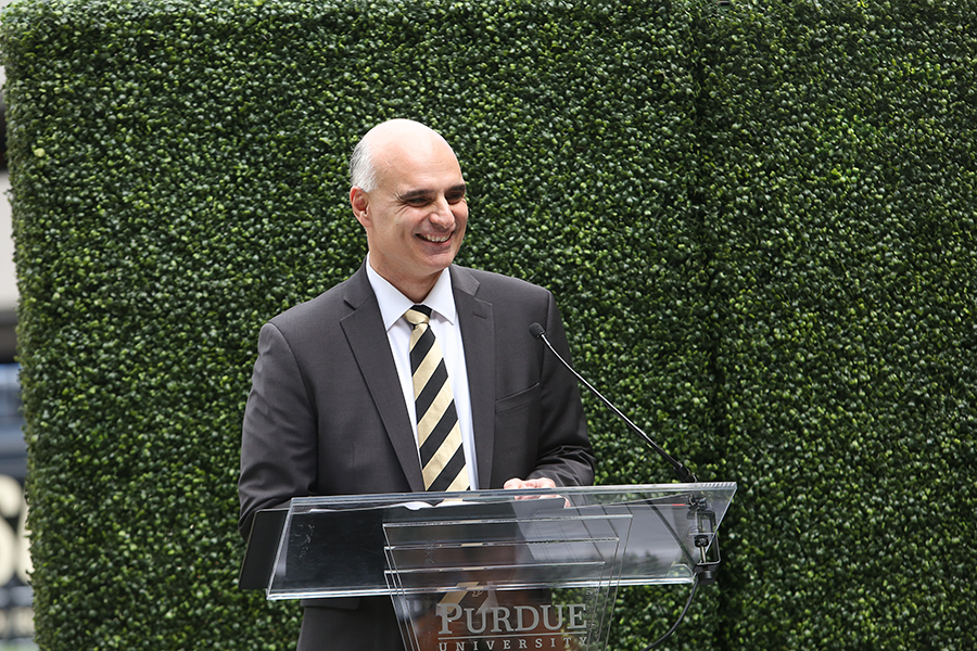 Photo of Dimitrios in front of a hedge wall speaking at a podium during the BHEE dedication event.