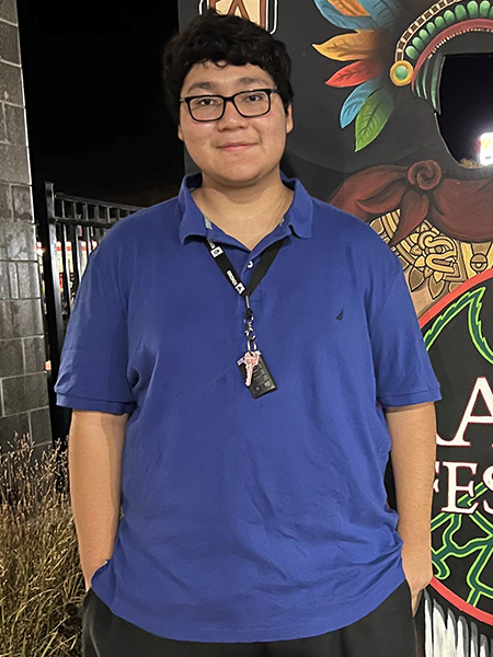 Student with dark hair smiling wearing glasses and blue shirt