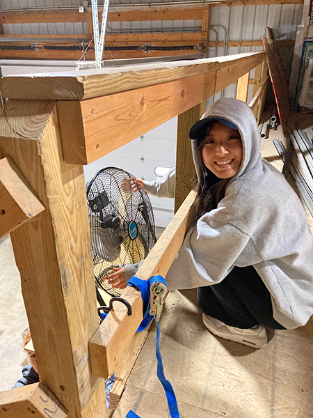 Student kneeling next to a wooden structure with a fan inside