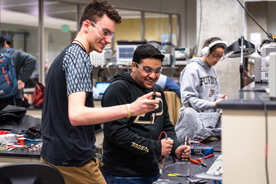 Two men holding cables and glass equipment, smiling.