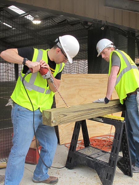 Two male students wearing construction gear drilling into a wood beam