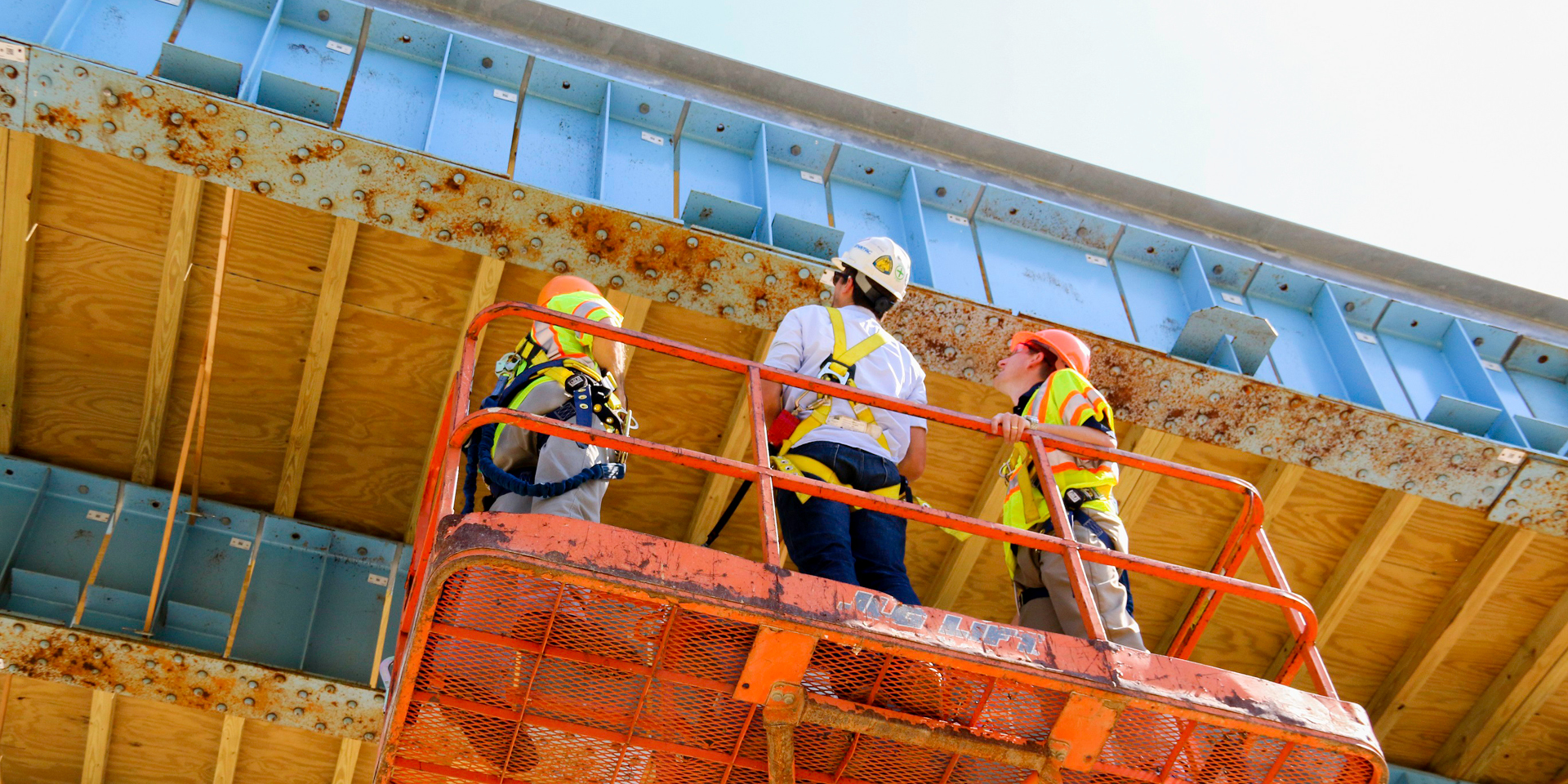 Three individuals with hard hats on looking at the underside of a bridge