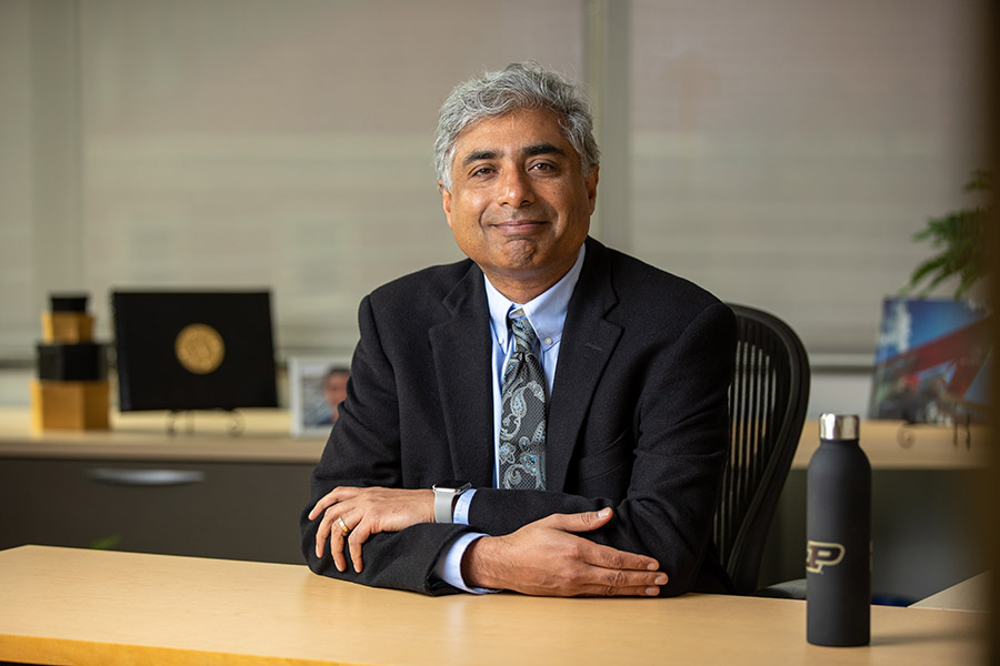 Dean Raman Arvind sitting at desk facing forward with arms crossed and smiling.