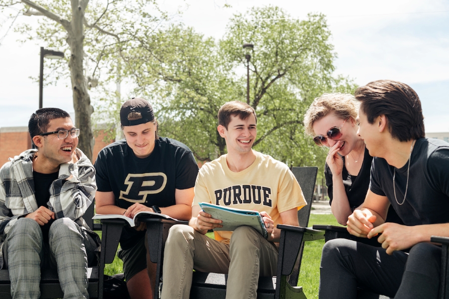 Photo of five students sitting together outside smiling with notepads.