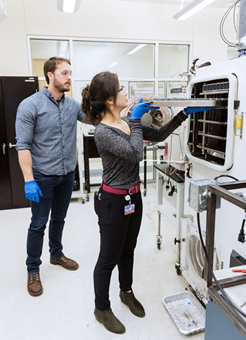 Photo of two students putting a tray into a machine.