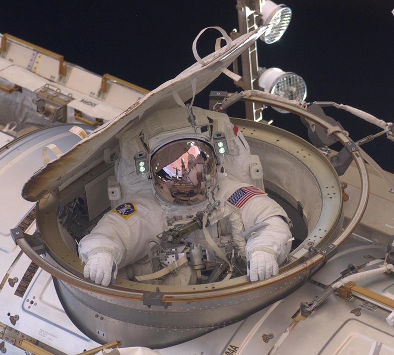 Drew Feustel in a space suit hanging half in and half out of the space station