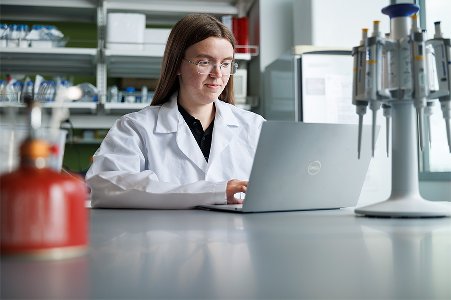 Amanda Wolf types on a laptop while wearing a white lab coat. 