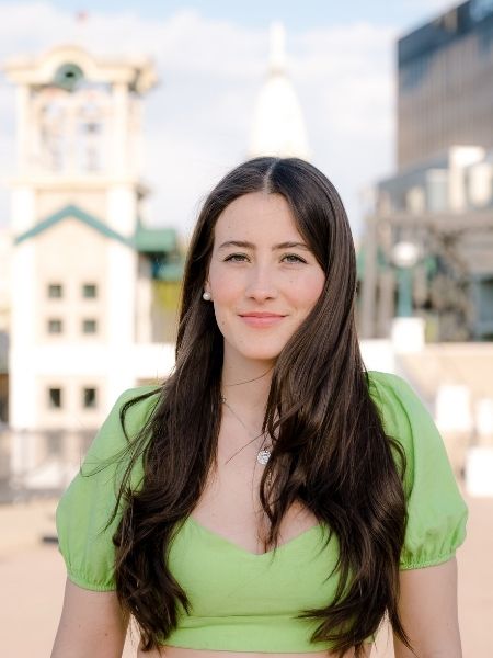 A portrait of Nora Miqueleiz-Alonso in a green shirt. Buildings in the background are blurred.
