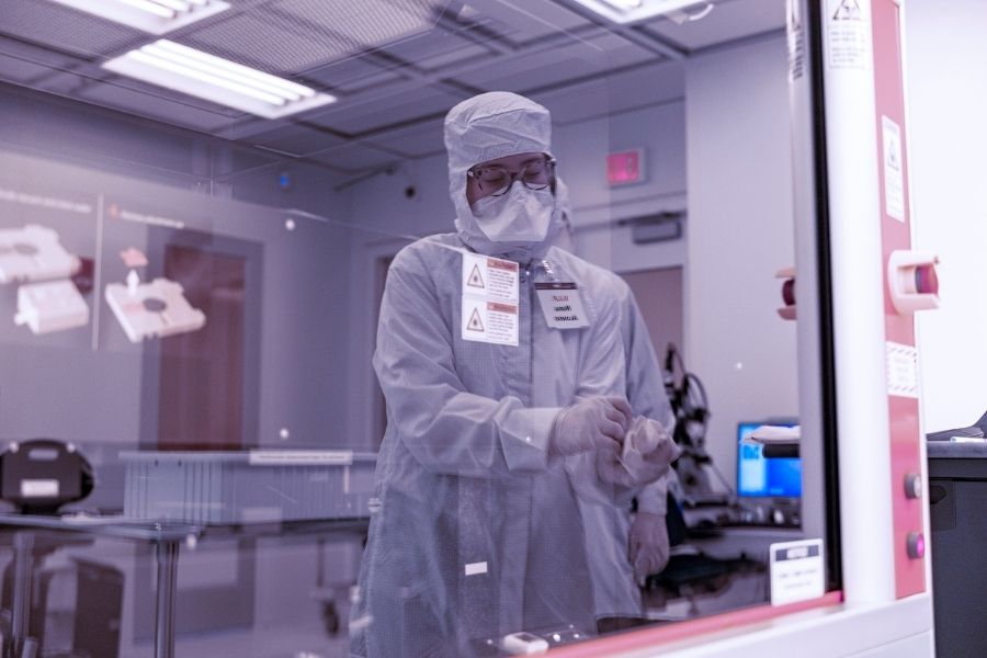 Nora Miqueleiz-Alonso is seen working in a cleanroom through the reflection of a piece of equipment’s window. Nora is covered from head to toe in a gown, hat, mask and gloves -- commonly referred to as a "bunny suit."