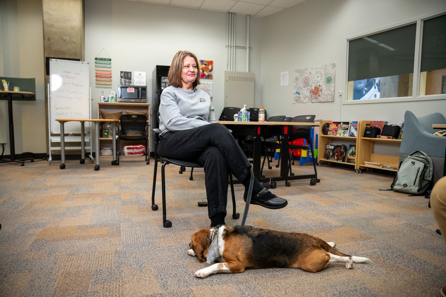Kristy Eaton, director of Purdue Engineering's CARES Hub, sits in the student well-being center in Neil Armstrong Hall of Engineering while Murphy, a beagle therapy dog, rests on the floor beside her.