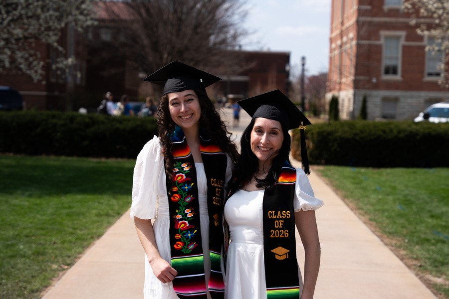 Karina Hollis-Brau, left, and Ariana Hollis-Brau, right, stand together in graduation caps and embroidered stoles on the Purdue University campus.