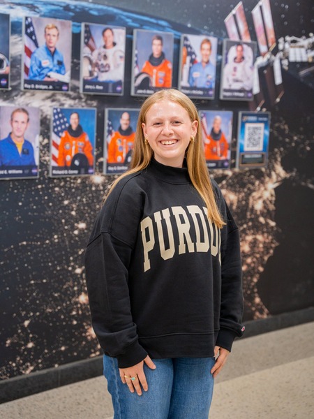 Purdue aerospace engineering junior Olivia DeScipio smiles in front of a wall of Purdue astronaut portraits.